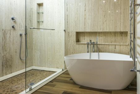 Contemporary bathroom featuring a marble wall, glass shower, and stylish bathtub.