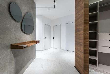 Interior of contemporary hall with mirrors and wooden shelf against big closet in spacious flat with doors and white walls
